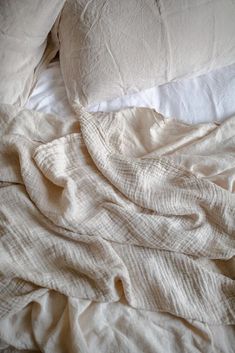 an unmade bed with white sheets and pillows