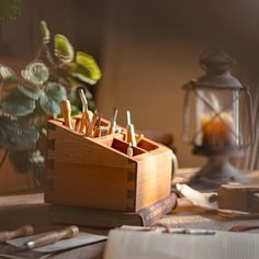 a wooden box filled with pens and pencils on top of a table next to a potted plant