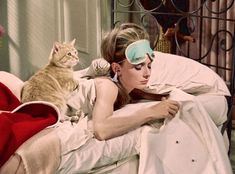 a woman laying on top of a bed next to a cat wearing a sleeping mask