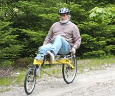 an older man is riding his bike down the road in front of some trees and bushes