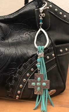 a black purse with a turquoise tassel hanging from it's side and a cross on the front