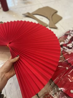 a person holding a red paper fan in their hand and some other items on the floor