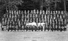 an old black and white photo of people in suits posing for a group photograph with trees in the background