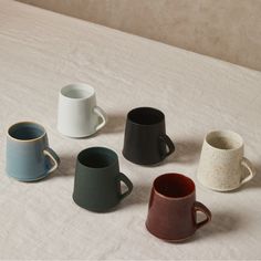 five different colored coffee mugs sitting on top of a white tablecloth covered bed