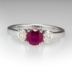 This pretty ring is centered with one (1) round mixed cut natural ruby set into a four-prong setting. The center stone is accented to each side by one (1) oval brilliant cut set into a four-prong setting. The ring measures 5.5mm at the top, rises 5.1mm above the finger, tapering to 2.2mm wide and 1.2mm thick at the base of the shank. This ring is currently a size 6.75. Classic Three Stone Ruby Ring With Diamonds, Luxury Oval Three-stone Ruby Ring, Classic Oval Lab-created Ruby Diamond Ring, Classic Three Stone Round Ruby Ring, Classic Diamond Ring With Lab-created Ruby Accent Stones, Formal Ruby Three Stone Ring With Diamonds, Classic Three Stone Ruby Promise Ring, Timeless Ruby Ring With Round Cut Center Stone, Elegant Three Stone Red Diamond Ring