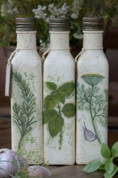 three bottles with herbs painted on them are sitting next to garlic and other vegetables in the background