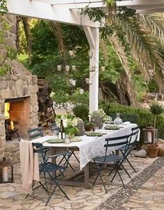 an outdoor dining area with stone fireplace and table set for four, surrounded by greenery