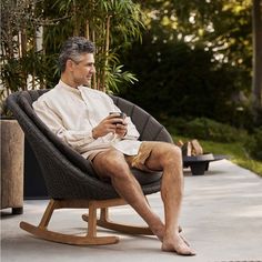 a man sitting in a rocking chair holding a cell phone and looking at his watch