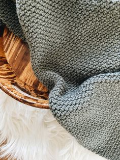 a wooden rocking chair covered in a gray and white knitted blanket next to a furry rug