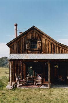 an old wooden building with chairs and tables in front of it on a grassy field