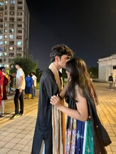 a man and woman standing next to each other in front of tall buildings at night