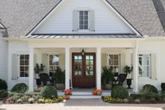 a white house with black shutters and pumpkins on the front porch, along with potted plants