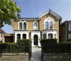 a large brick house with white trim on the front door and windows, surrounded by hedges