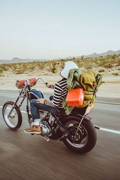 a man riding on the back of a motorcycle down a road with backpacks strapped to it