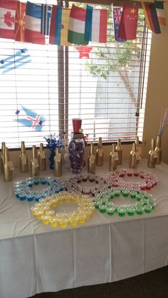 a table topped with lots of cups and vases next to a window filled with flags