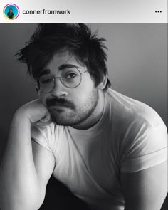 a black and white photo of a man with glasses looking at the camera while sitting down