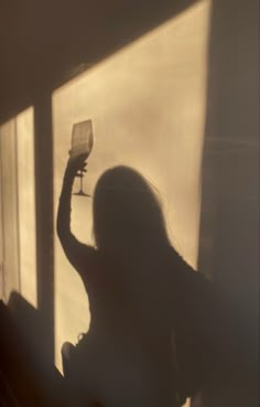 a woman standing in front of a window holding a wine glass up to her face