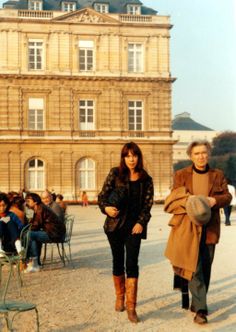 two people walking in front of a large building with lots of people sitting on chairs