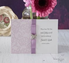 a vase filled with pink flowers next to a purple and white greeting card on top of a table