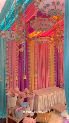 a decorated canopy bed with pink, blue and yellow drapes on the ceiling above it