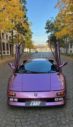 a purple sports car parked on the side of a road next to trees with its doors open