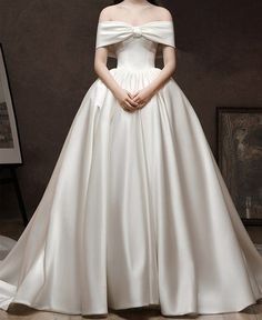 a woman in a white wedding dress standing next to a painting on the wall with her hands behind her back