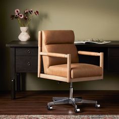 a brown leather office chair sitting on top of a wooden desk next to a vase with flowers