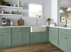 a kitchen with green cabinets and white counter tops, wooden flooring and open shelving