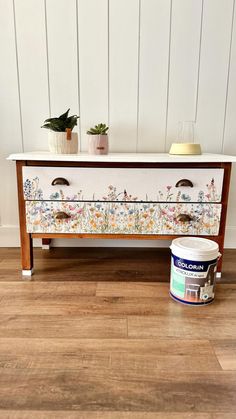 a white painted dresser sitting on top of a wooden floor next to a potted plant