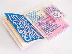 an open book with pink and blue writing on it's cover, sitting on a white surface