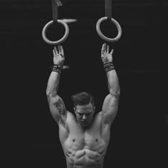 a shirtless man holding two rings above his head