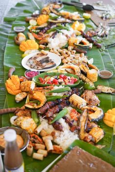 a long table filled with lots of food on top of a green leaf covered table