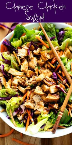 a salad with chicken, carrots and lettuce in it on a wooden table