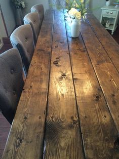 a wooden table with chairs around it and flowers in a vase on the table top