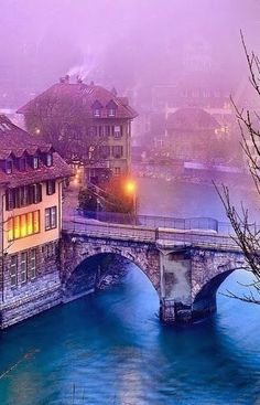 a bridge over a body of water with buildings in the background and foggy sky