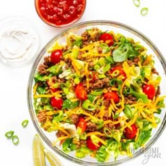 a salad with cheese, tomatoes and meat in a glass bowl on a white table