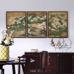 three paintings hang on the wall above a dining room table with chairs and a vase filled with flowers