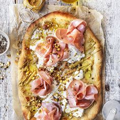 a pizza sitting on top of a wooden table next to glasses of wine and condiments