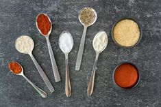 six spoons with different types of seasoning in them on a gray table top