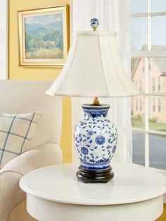 a blue and white vase sitting on top of a table next to a lamp in front of a window