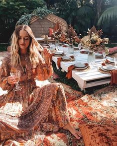 a woman sitting at a table with plates and glasses in front of her, surrounded by greenery