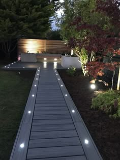 a walkway lit up at night with lights on it and some trees in the background