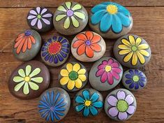 painted rocks with flowers on them sitting on a wooden surface