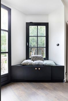 a window seat with pillows on it in front of a wooden floor and black framed windows