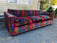 a multicolored couch sitting in front of a house on the side of a road