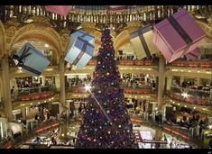 a large christmas tree in the middle of a mall with presents hanging from it's sides