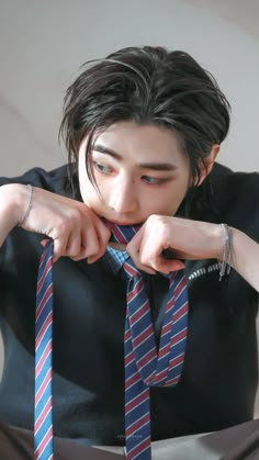 a young man wearing a black shirt and blue striped tie with his hands on his chin