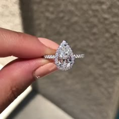 a woman's hand holding an engagement ring with a pear shaped diamond on it