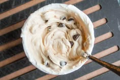 a bowl filled with cream and chocolate chips on top of a wooden table next to a spatula