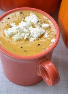 a close up of a cup of soup with cheese on top and an orange in the background